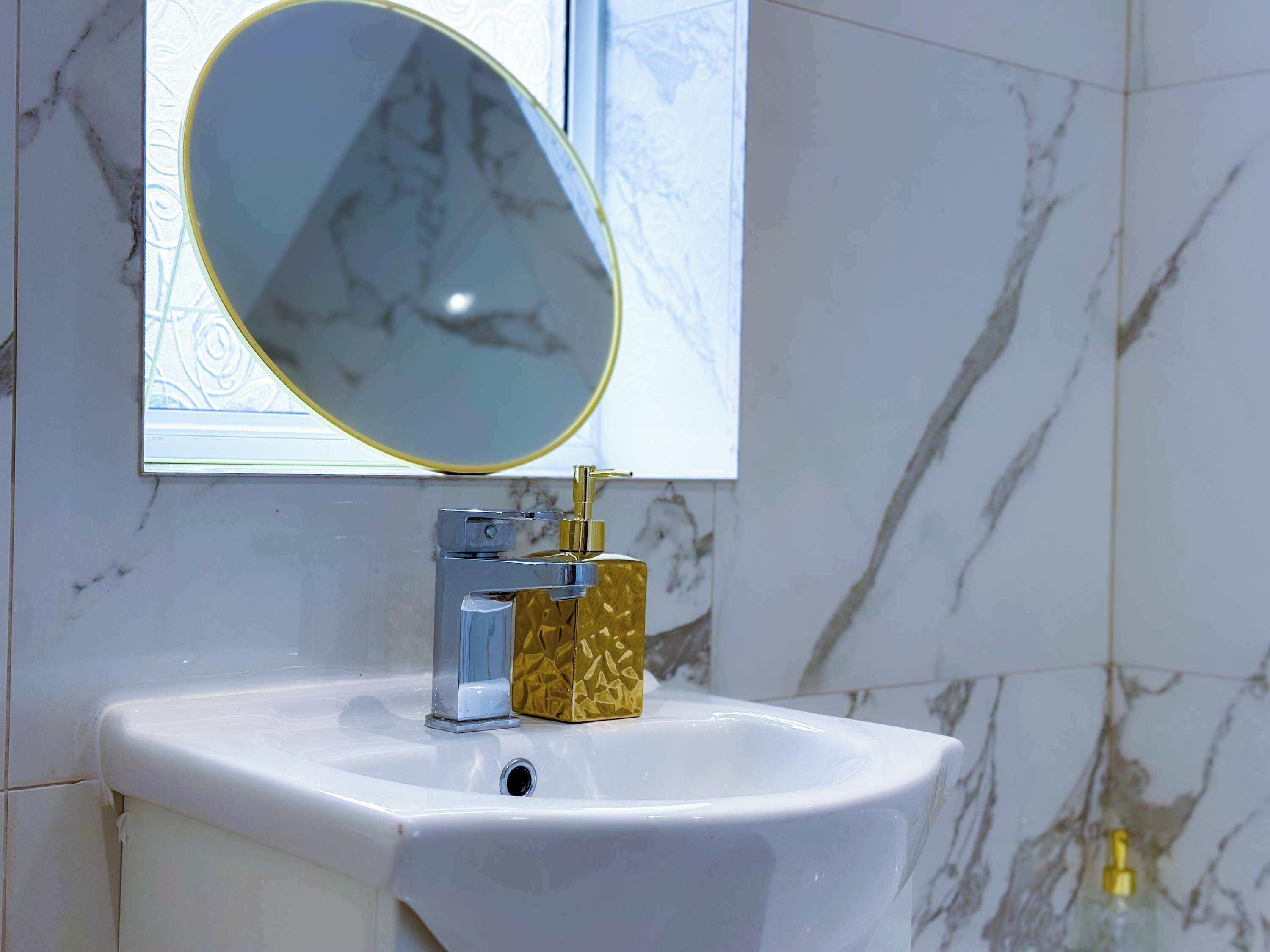A bathroom with a white sink, a gold soap dispenser, and a mirror with a gold frame.