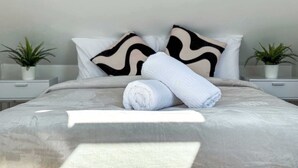 A neatly made bed with a rolled towel, two decorative pillows, and two potted plants on bedside tables. - Stylish Apartment in Buckhurst Hill (London)