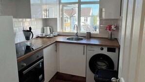 A compact kitchen with a built-in oven, a washing machine, and a window providing a view of the neighborhood. - Stylish Apartment in Buckhurst Hill (London)