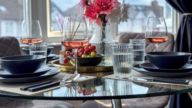 A table set for two with wine glasses, a vase with flowers, and a bowl of fruit. - Stylish Apartment in Buckhurst Hill (London)