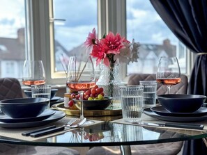 A table set for two with wine glasses, a vase with flowers, and a bowl of fruit. - Chic Apartment w/ Fast London Access & WiFi (London)