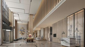 Un lobby espacioso con techo alto, una recepción, zona de estar y una pared decorativa con paneles verticales.