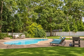 Ein Garten mit Swimmingpool, Liegestühlen und Grill.