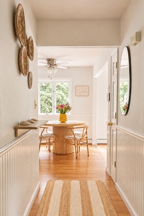 A hallway leading to a dining area with a round table, chairs, and a ceiling fan. - Heated Pool, Gym & Game Room, 5 Min to Beach (Hampton Bays)