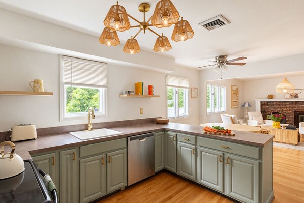 A modern kitchen with a central island, built-in appliances, and a dining area with a fireplace. - Heated Pool, Gym & Game Room, 5 Min to Beach (Hampton Bays)