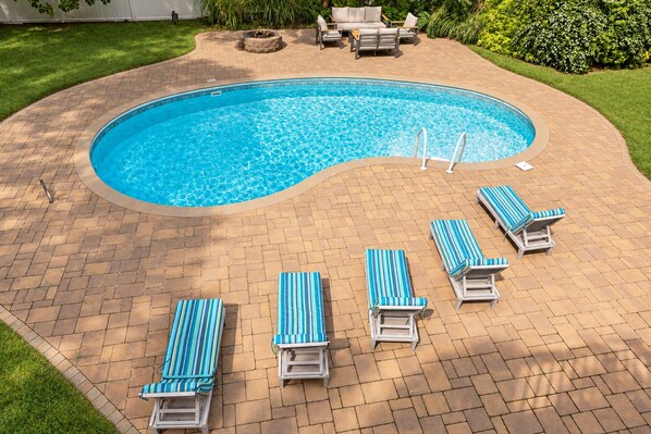A swimming pool with a curved edge, surrounded by a brick patio. There are six lounge chairs with striped cushions. - Heated Pool, Gym & Game Room, 5 Min to Beach (Hampton Bays)