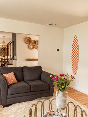 A living room with a dark grey sofa, a glass coffee table, and a vase with flowers.
