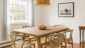 A dining area with a wooden table and chairs, a hanging light fixture, a window with curtains, and a framed picture on the wall. - Hampton Gem: Heated Pool, BBQ, 5 Min to the Beach (Hampton Bays)