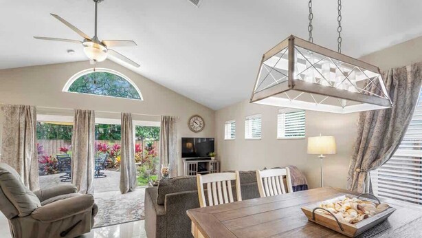 A spacious living room with a dining area, a ceiling fan, and a large window overlooking a garden.