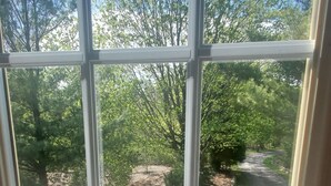 A view through a window with a wooden deck and a paved path leading to a wooded area. - Large studio apartment in charming Elk Rapids. (Elk Rapids)