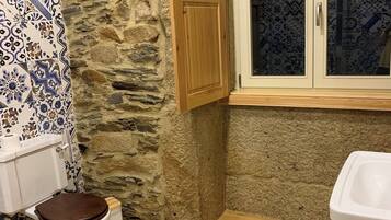 A bathroom with a stone wall, a wooden cabinet, a toilet, a sink, and patterned tiles.