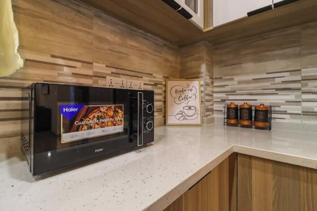 Een keuken met een moderne magnetron, een bord met een koffie-thema en drie flessen op het aanrecht.