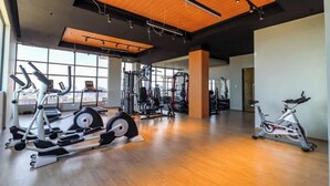 Et rummeligt fitnesscenter med løbetræningsmaskiner, styrketræningsudstyr og et stort vindue, der giver naturligt lys.