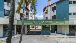 Un edificio con un letrero que dice 'BLUE GARDEN 5933' y un acceso pavimentado con palmeras.