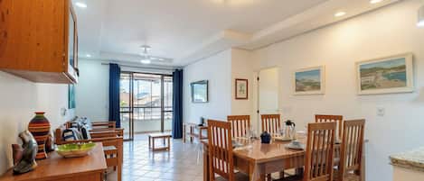 Angolo ristoro con tavolo e sedie in legno, bancone cucina con oggetti decorativi e vista panoramica attraverso una porta in vetro.