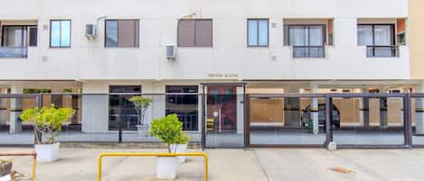 A multi-story building with a ground-level entrance, potted plants, and a yellow barrier.