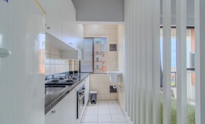 Une cuisine étroite avec des meubles blancs, un plan de travail noir et une fenêtre donnant sur un immeuble.
