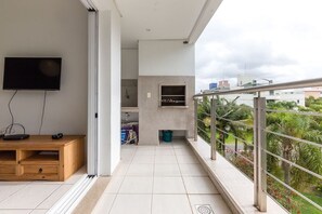 Un balcón con televisor, muebles de madera y una zona de cocina.