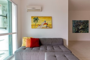 Un sofá gris con dos almohadas, un cuadro de una escena tropical y otro cuadro en la pared.