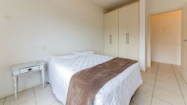 A bedroom with a bed, a nightstand, a wardrobe, and an air conditioning unit on the wall.