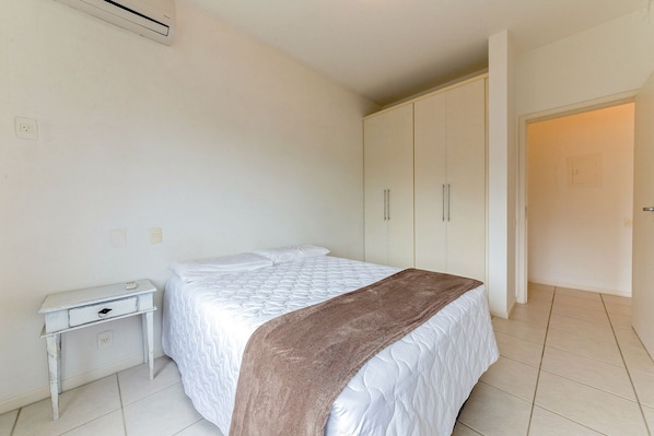 A bedroom with a bed, a nightstand, a wardrobe, and an air conditioning unit on the wall.
