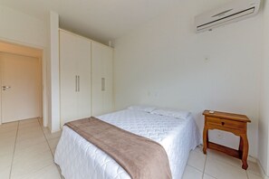 A bedroom with a bed, a bedside table, a wardrobe, and an air conditioning unit.