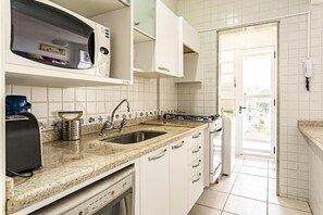 Cocina con gabinetes blancos, microondas, fregadero y lavavajillas.