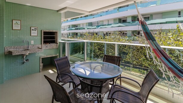 En balkon med et glasbord og stole, en hængekøje og udsigt til en bygning med balkoner.