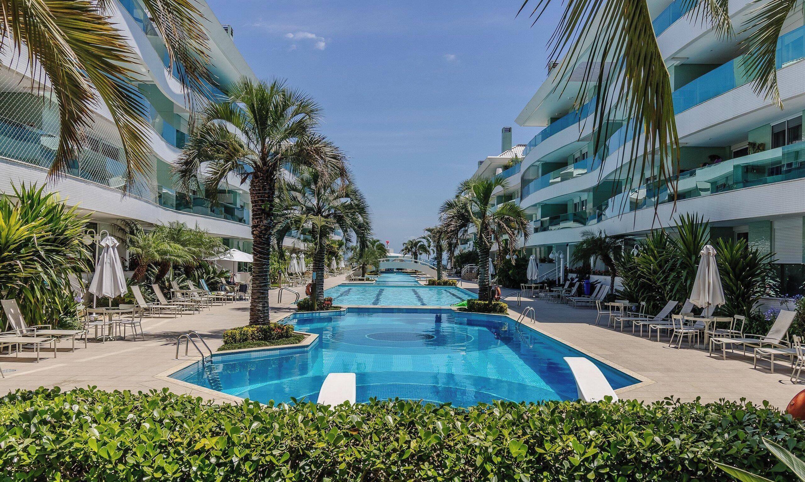 Ein modernes Hotel mit einem zentral gelegenen Schwimmbecken, umgeben von Palmen und Liegestühlen.