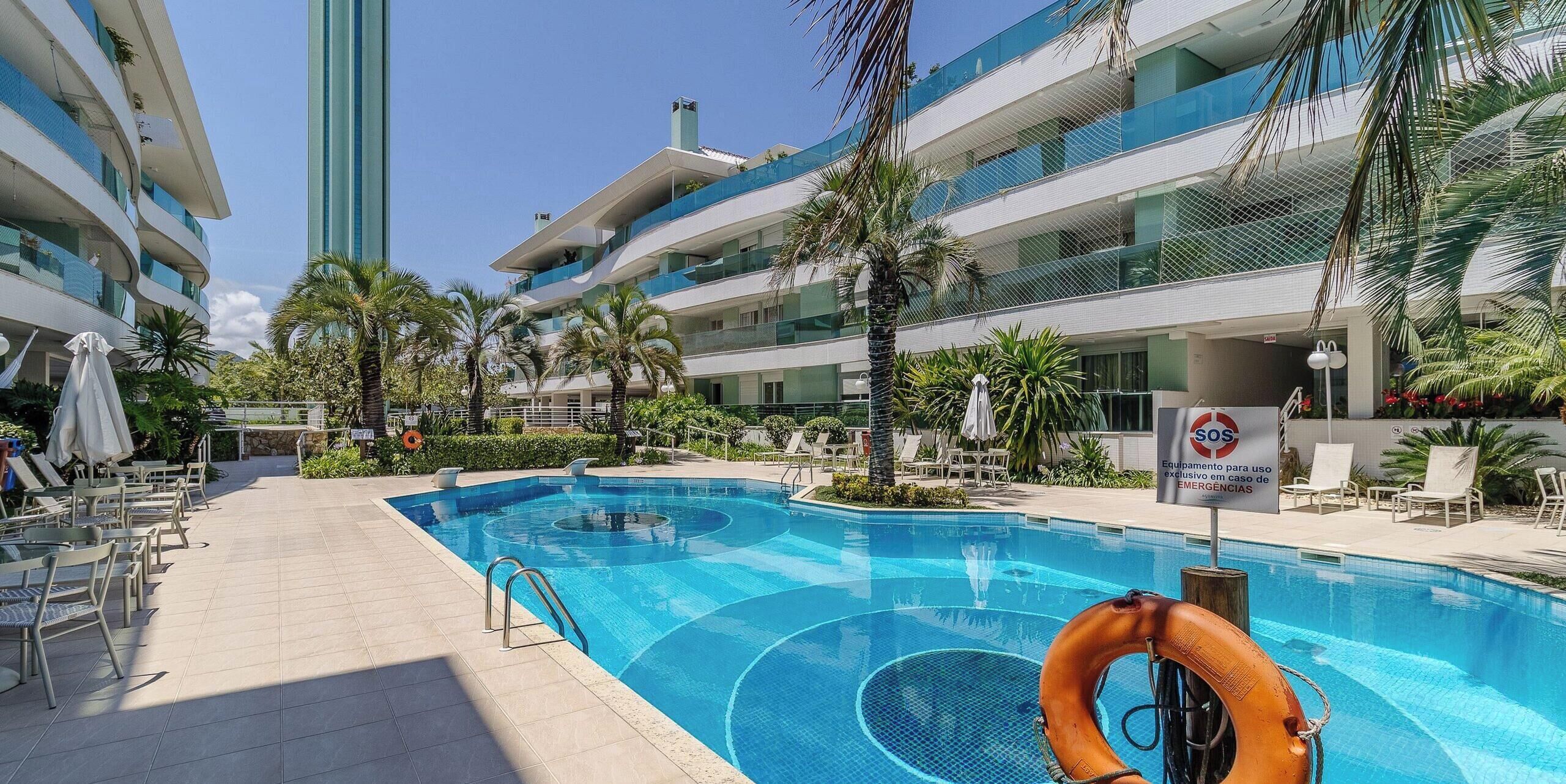 A swimming pool with a lifebuoy, lounge chairs, and a sign indicating emergency equipment.