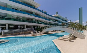 Ein modernes Hotel mit Schwimmbad, mehreren Balkonen und einer Brücke, die verschiedene Ebenen miteinander verbindet.