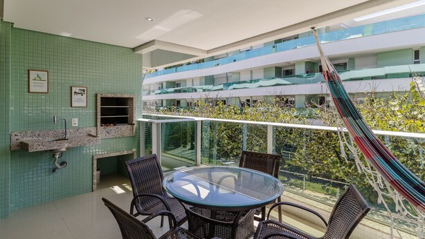 Uma varanda com mesa e cadeiras de vidro, uma rede e vista para um edifício com varandas.