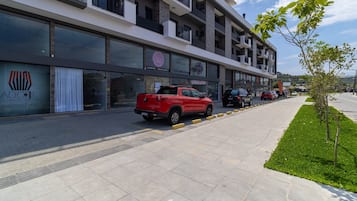 Un edificio moderno de varios pisos, con locales comerciales y una camioneta roja estacionada en la acera.