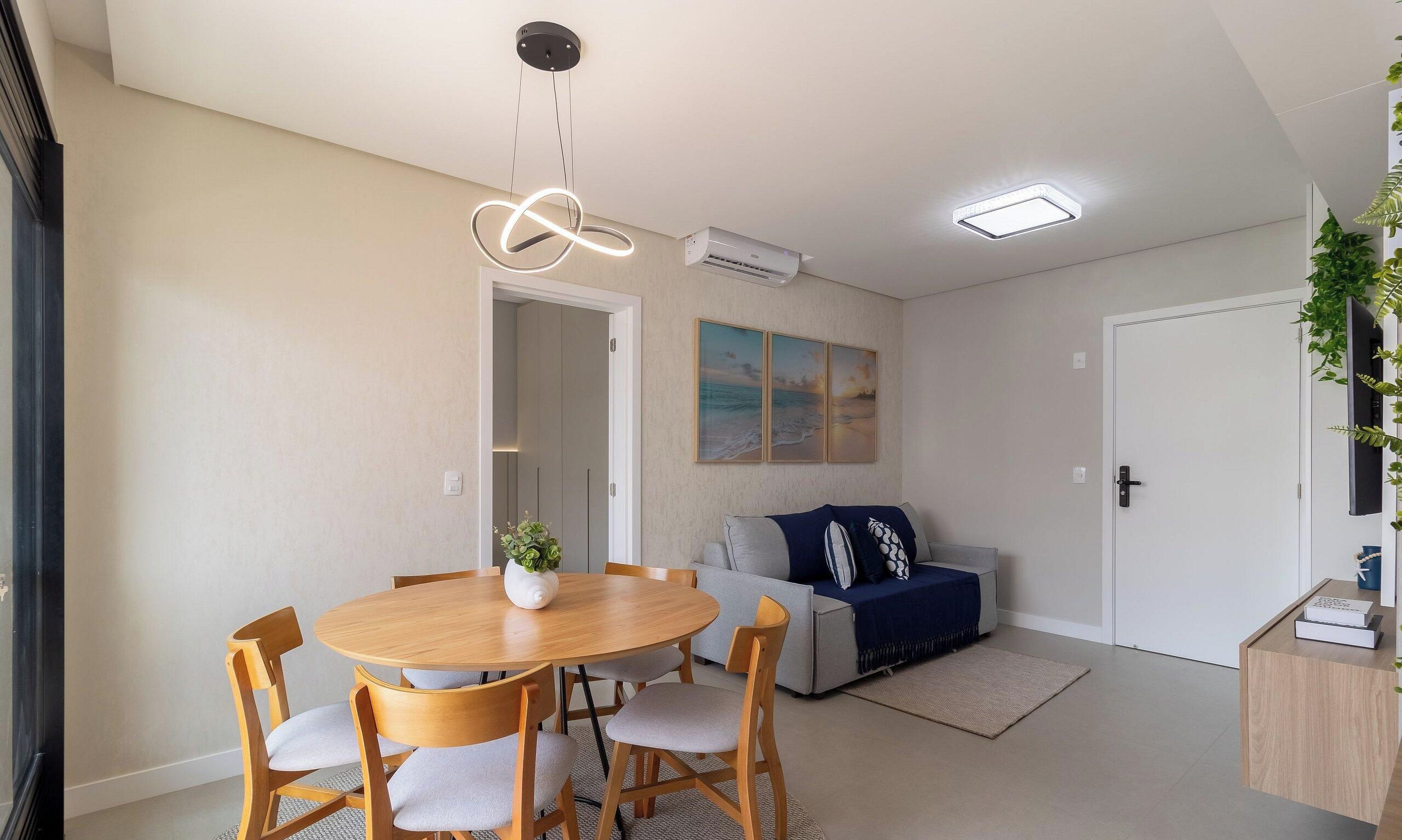 Una sala de estar moderna con una mesa de comedor redonda de madera, un sofá gris y un televisor sobre un mueble.