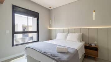 Un dormitorio moderno con una cama grande, mesitas de noche, una ventana y una lámpara de pared.