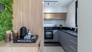A modern kitchen with a wooden wall, a black countertop, and stainless steel appliances. - Modern Apartment Near the Beach! - Atc0301 (Florianópolis)