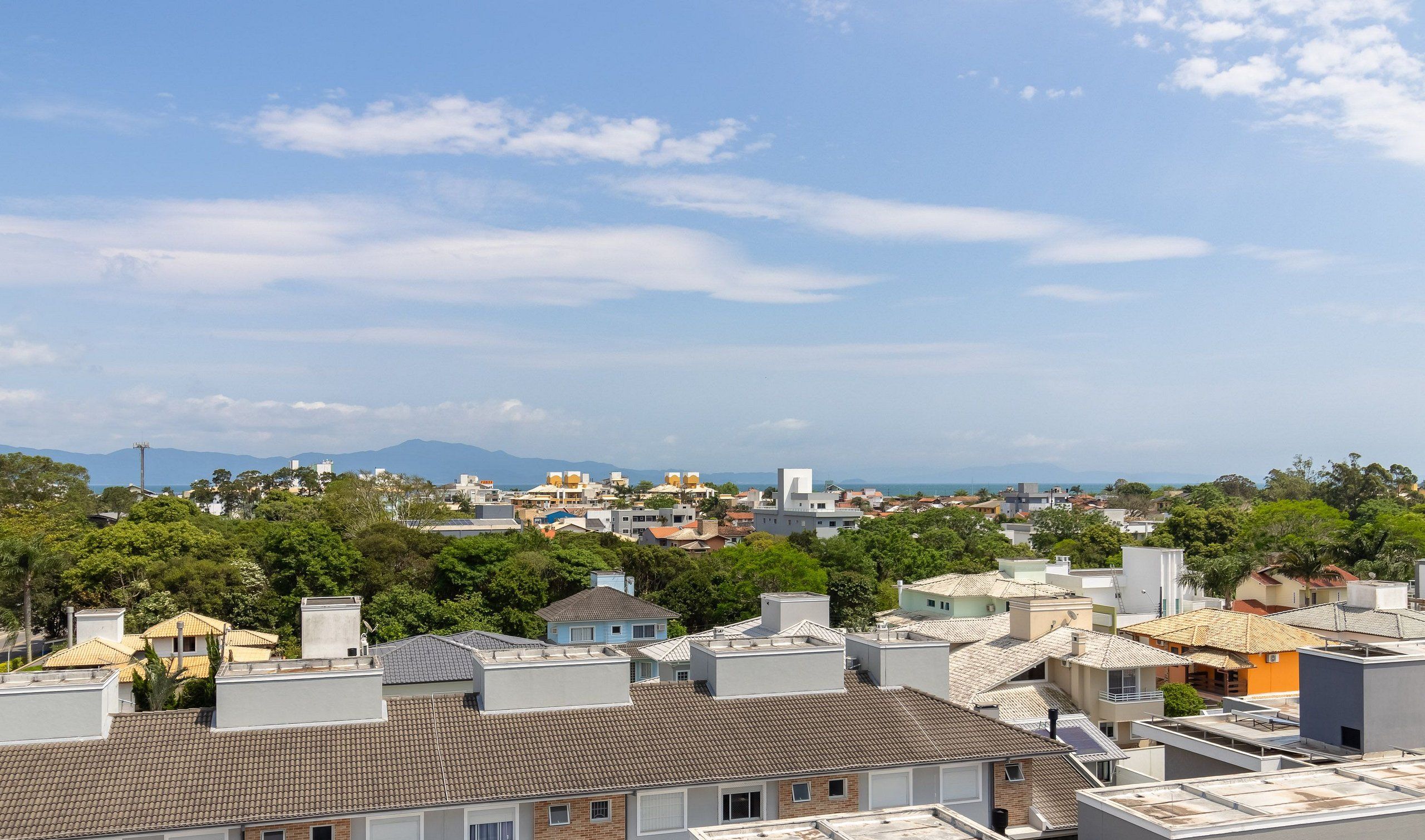 A residential area with various buildings, including houses with tiled roofs and some with flat roofs, surrounded by greenery.