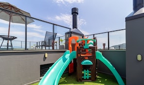 Un área de juegos en la azotea con un tobogán, una estructura para escalar y una chimenea.