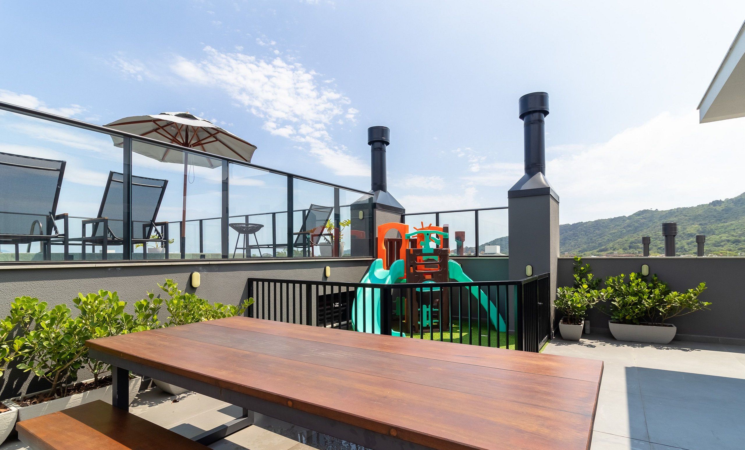 A rooftop terrace with a wooden table, chairs, a children's play area, and a view of the surrounding landscape.