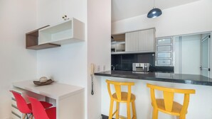 Une cuisine moderne avec un plan de travail noir, des appareils en acier inoxydable et un luminaire suspendu bleu.