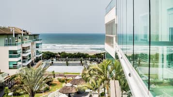 Um hotel moderno com vista para o oceano, área de piscina com palmeiras e uma construção com telhado de palha.