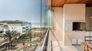 A balcony with a view of the sea and buildings, a wooden ceiling, and a kitchen area with a stone backsplash. - Beachfront Apartment w/ View Beach Santinho Asr204 (Florianópolis)