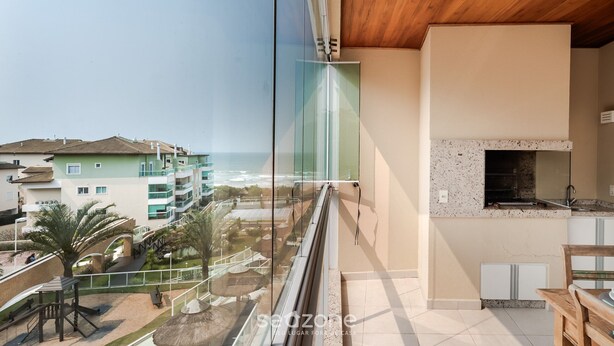 Un balcon avec vue sur la mer et les bâtiments, un plafond en bois et un coin cuisine avec un pare-feu en pierre.