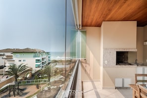 Ein Balkon mit Blick auf das Meer und Gebäude, eine Holzbalkendecke sowie ein Küchenbereich mit Steinrückwand.