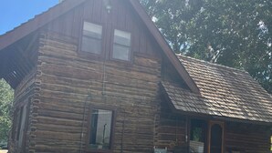 Une cabane rustique en rondins de bois, dotée d’une terrasse en bois et de deux chaises à l’extérieur.