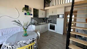 A compact kitchen with white cabinets, a microwave, and a sink. There's a dining area with a table and chairs, and a staircase leading to an upper level. - Le Mezmarine - Front de Mer (Bray-Dunes)