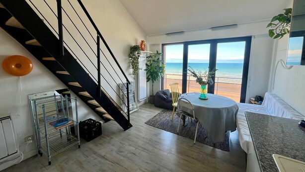 A modern living room with a staircase, a dining area, and a large window offering a view of the beach. - Le Mezmarine - Front de Mer (Bray-Dunes)