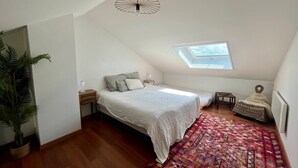 A small, well-lit attic bedroom with a skylight, a bed with white linens, a colorful rug, and a potted plant. - Le Mezmarine - Front de Mer (Bray-Dunes)