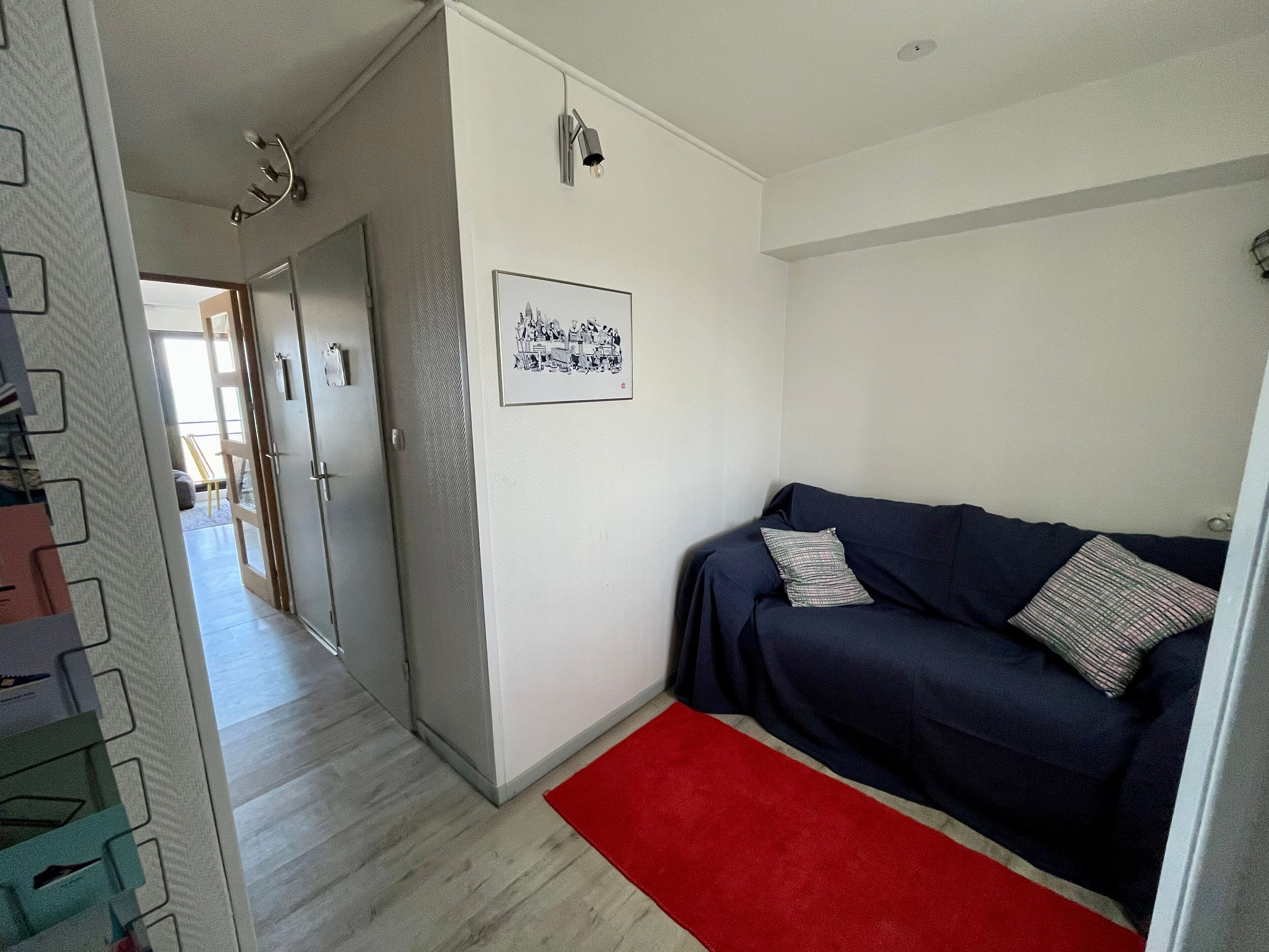 Ein modernes Wohnzimmer mit einem dunkelblauen Sofa, einem roten Teppich und einem gerahmten Bild an der Wand.