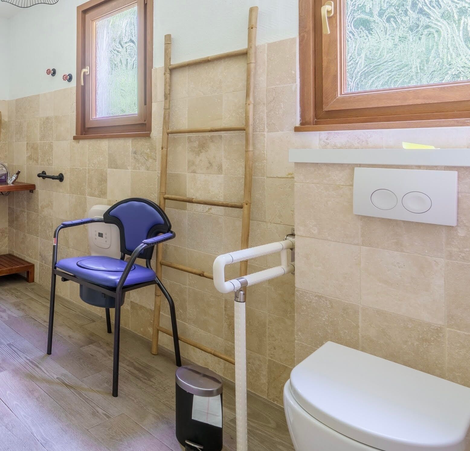 A bathroom with a toilet, a blue chair, a wooden ladder, and a window with frosted glass.
